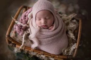Newborn baby girl in pink wrap in basket