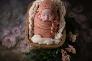 Newborn girl in orange wrap with floral background