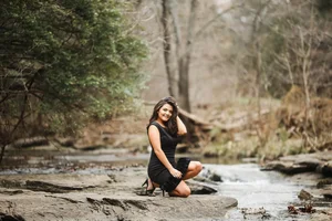 Senior portrait in black dress on river rocks