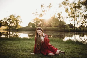 Senior portrait in red dress by lake at sunset